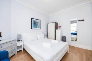 a white bedroom with a large bed and a dresser at Charing Cross Road One Bedroom in London