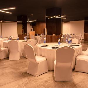 Cette chambre comprend des tables et des chaises blanches ainsi que des bouteilles d'eau. dans l'établissement Vertigo Hotel, à Lagos