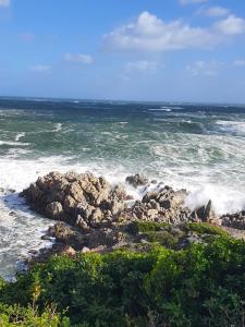 eine Gruppe von Felsen im Ozean mit Wellen in der Unterkunft KUSVAALBOS SELFSORG WOONSTEL in De Kelders