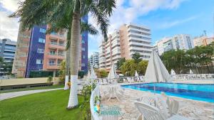 a pool with white chairs and a palm tree at Alugar na Riviera Boulevard Flat in Riviera de São Lourenço