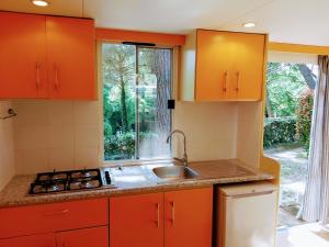 una cocina con armarios naranjas, fregadero y ventana en Holiday Travel Genius at Toscana Holiday Village Camping, en San Romano