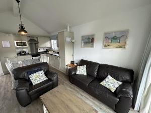 a living room with two leather couches and a kitchen at Sea-Renity - Part of the The Bay Filey Holiday Village with pool, gym and direct beach access, pub, restaurant, tennis and meadows walks in Filey