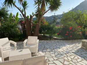a patio with white chairs and a tree and flowers at A Vista in Parga