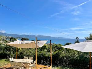 una mesa y sillas con sombrillas y el océano en Maison en bord de mer en Coggia