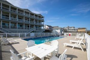 a pool with white tables and chairs next to a hotel at SC202 Coastal LegaSea in Kill Devil Hills