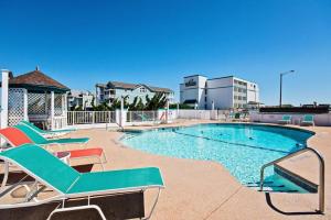 a swimming pool with chaise lounge chairs next to a building at CR201 Salty Tides in Kill Devil Hills