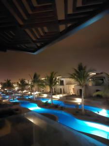 - une piscine avec des palmiers et des lumières la nuit dans l'établissement Hawana Salalah - Riviera NEW, à Salalah