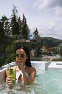 una donna seduta in piscina con un drink di Bukville Hotel & SPA a Bukovel