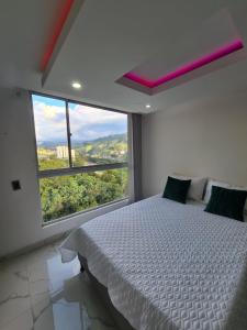 a bedroom with a white bed and a large window at Moderno apartamento con vista a las montañas in Manizales