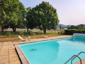 una gran piscina con 2 sillas de césped y árboles en La Magnanerie en Portes-en-Valdaine