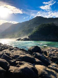 a rocky beach with the ocean and mountains in the background at Pouso da Celeste - Trindade in Trindade