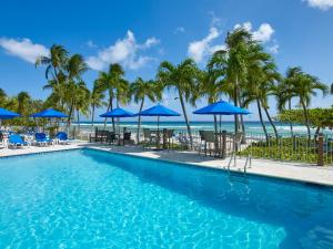 a swimming pool with palm trees and blue umbrellas at Coconut Court Beach Hotel in Bridgetown
