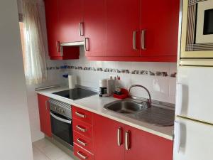 a kitchen with red cabinets and a sink at Seaside apartment with balcony in Las Galletas