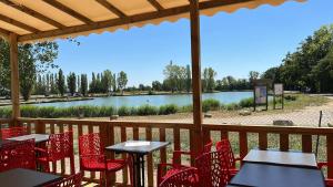 a patio with red chairs and tables and a lake at L'Oasis des Dombes in Ambérieux-en-Dombes