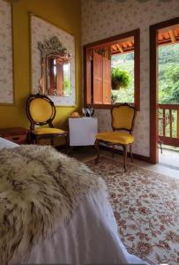 a bedroom with a bed and two chairs and a mirror at Pousada Sítio das Pedras in Domingos Martins