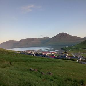 a green hillside with a town and a body of water at Experience unique Faroe Islands holiday home by the sea with great views, fully equipped kitchen and reliable Wi-Fi 