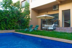 a swimming pool with chairs and an umbrella next to a house at New villa in Marrakech palmeraie in Marrakech