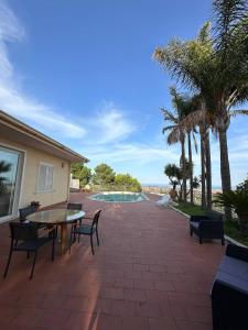 eine Terrasse mit einem Tisch, Stühlen und einem Pool in der Unterkunft Holiday flower villa panoramica sul golfo di Catania in Misterbianco