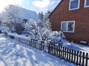 ein mit Schnee bedeckter Zaun vor einem Haus in der Unterkunft Ferienhaus La Farfalla in Munster im Heidekreis