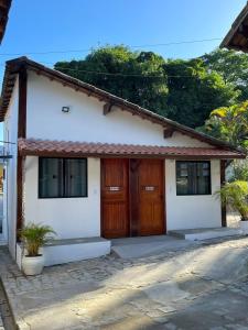 a small white house with wooden doors and windows at Pousada Rosa dos Ventos Kchu in Cachoeiras de Macacu