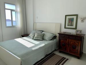 1 dormitorio con 1 cama con mesita de noche de madera y ventana en Apartamento vista do mar, pé na areia e águas tranquilas, no cento de Guarapari en Guarapari