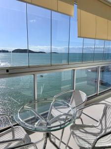 einen Glastisch und Stühle auf einem Balkon mit Meerblick in der Unterkunft Apartamento vista do mar, pé na areia e águas tranquilas, no cento de Guarapari in Guarapari