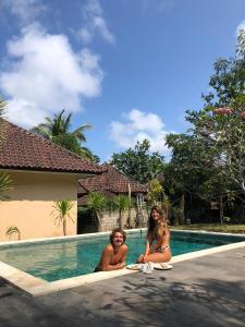 Dos mujeres en traje de baño sentadas junto a una piscina en Join Homestay, en Kuta Lombok