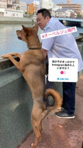 un hombre de pie junto a un perro con un cartel en él en オーベルジュ鳴門, en Naruto