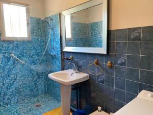 La salle de bains est pourvue de carrelage bleu, d'un lavabo et d'une douche. dans l'établissement Casa Minnana, à Figari