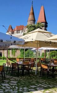 a restaurant with tables and umbrellas in front of a castle at Hanul Huniazilor in Hunedoara