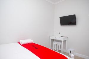 ein weißes Zimmer mit einer roten Decke auf einem Bett und einem Schreibtisch in der Unterkunft RedDoorz Plus @ Harmonie Cepu Blora in Cepu