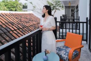 una donna in piedi su un balcone con un drink di De An Hotel a Hoi An