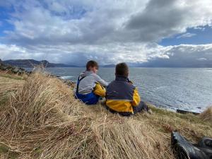 Dos chicos sentados en una colina con césped y vistas al agua en Stad Accommodation en Stokke