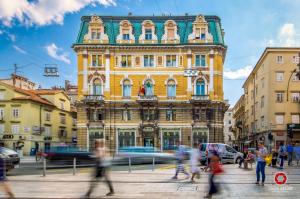 un grand bâtiment jaune avec des gens qui marchent devant lui dans l'établissement El Caminante Apartment, à Rijeka