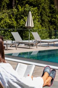une femme assise sur une chaise en lisant un livre à côté d'une piscine dans l'établissement Aktivhotel Waldhof, à Oetz