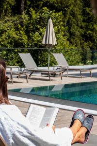 Kobieta leżąca na krześle czytająca książkę obok basenu w obiekcie Aktivhotel Waldhof w mieście Oetz