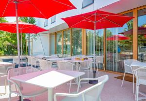 une rangée de tables et de chaises avec des parasols rouges dans l'établissement greet hotel Salon de Provence, à Salon-de-Provence