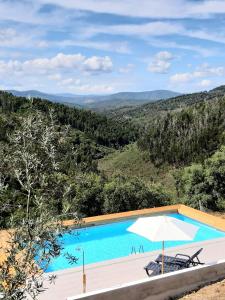 a swimming pool with an umbrella and a view of the mountains at Retiro da Cava, piscina privada in Oleiros