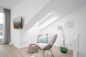 a white living room with a chair and a tv at SEASIDE - Neubau mit Meeresblick in Sierksdorf