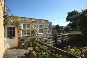 a stone cottage with a white door and flowers at Holmlea in Mickleton