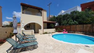 een zwembad met stoelen en een parasol en een huis bij Villa Elaia in Almirida