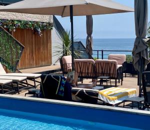 a swimming pool with chairs and an umbrella and the ocean at Les Alcyons in Le Lavandou