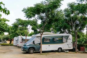 Camping La Llosa في كامبريلس: سيارة فان خضراء وبيضاء متوقفة أمام شاحنين