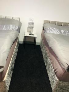 two beds in a room with a side table at Modern Travis House in Burnley
