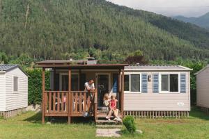 un homme et deux enfants debout sur la terrasse couverte d'une petite maison dans l'établissement Sarca Lodge Val Rendena, à Dare