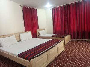 Chitral Inn Resort (Kalash Valley) في شيترال: غرفة نوم بسريرين وستائر حمراء