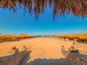 a beach with some straw umbrellas and the ocean at Flight Mode Camp in Nuweiba