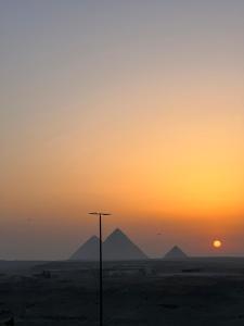 una puesta de sol en el desierto con montañas en el fondo en Pyramids Desert Gate Hotel en ‘Ezbet `Abd el-Ḥamîd