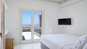 a white bedroom with a bed and a window at Home of the Gecko - Mykonos Town in Megali Ammos