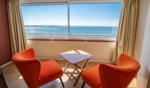 een kamer met 2 stoelen, een tafel en een groot raam bij LOGIS HOTEL - La Petite Rade in Le Havre